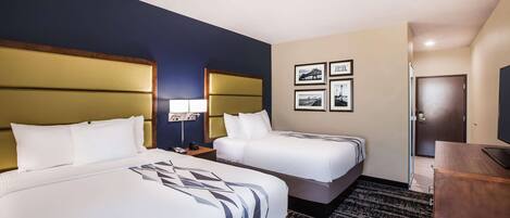 A hotel room with two beds, a desk, a TV, and framed pictures on the wall.