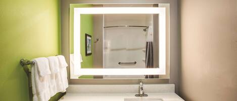 A bathroom with a white sink, a large mirror, and a shower visible in the reflection.
