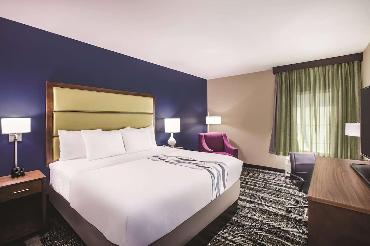 Une chambre d’hôtel avec un grand lit, deux tables de chevet avec des lampes, un bureau, une chaise et un téléviseur.