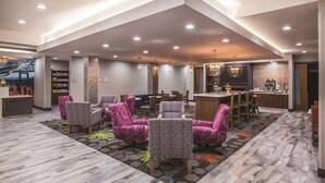 A spacious lobby with modern seating, a reception area, and a kitchen visible in the background. - La Quinta Inn & Suites by Wyndham Baton Rouge - Port Allen (Port Allen)