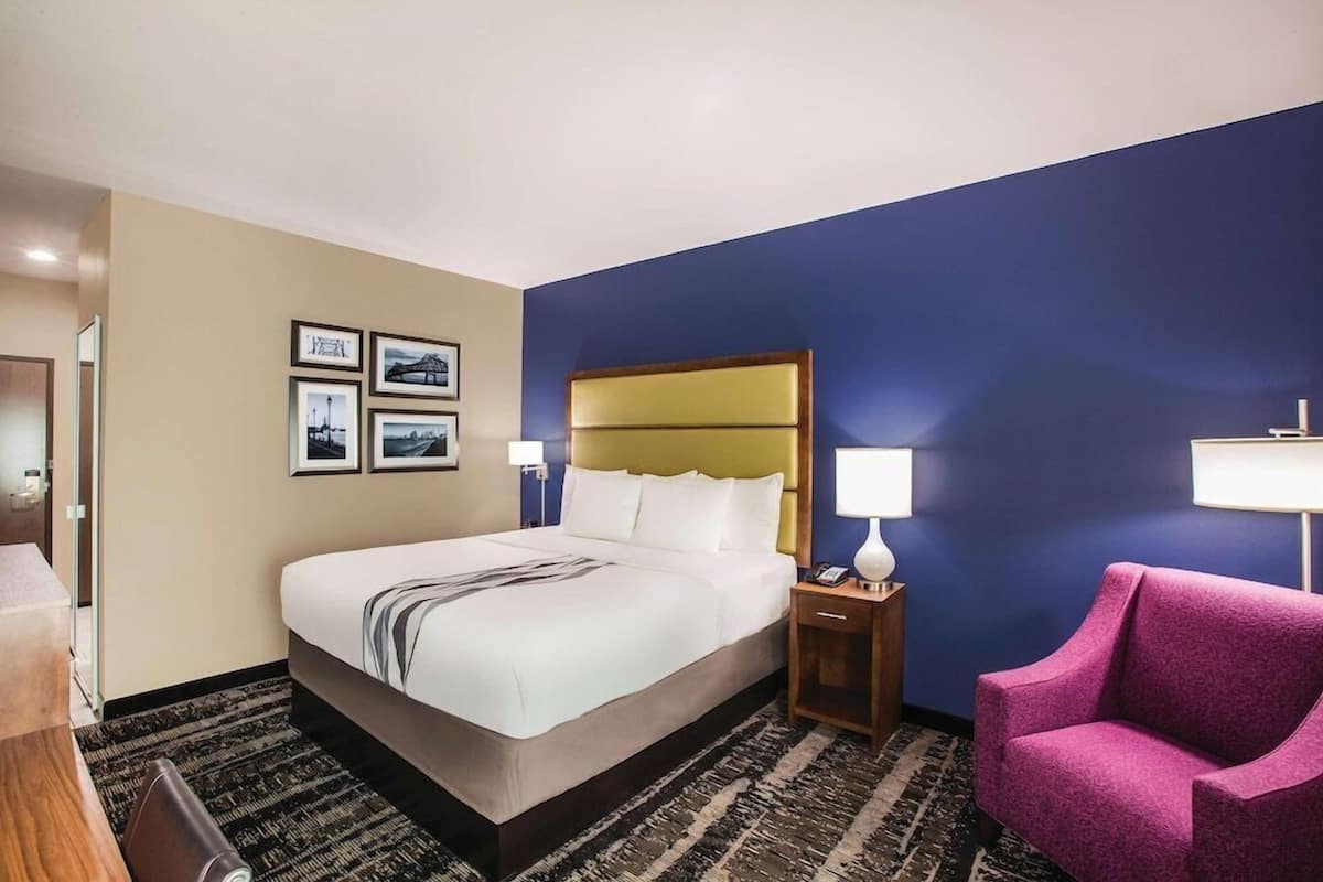 Une chambre d’hôtel avec un grand lit, une table de chevet avec une lampe, une chaise et des tableaux encadrés au mur.