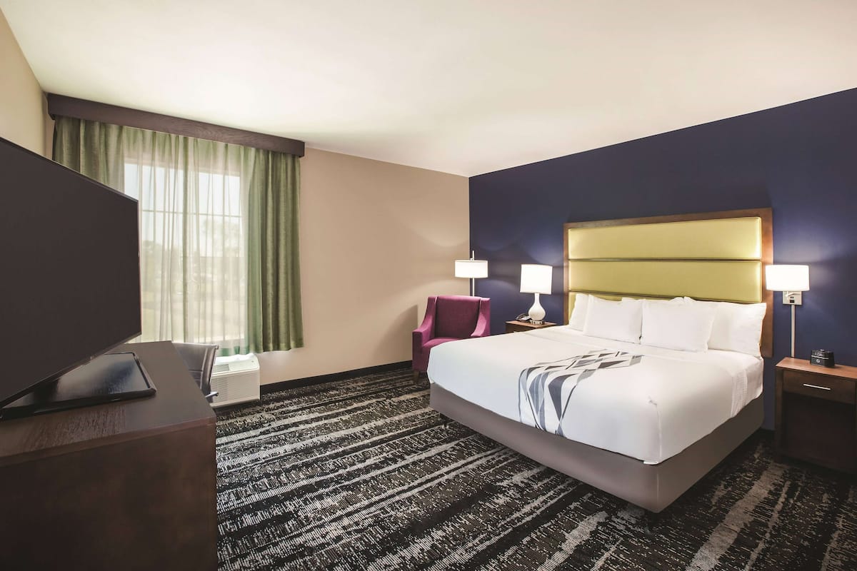 Une chambre d’hôtel avec un grand lit, deux lampes de chevet, un bureau avec un téléviseur à écran plat, une chaise et une fenêtre avec des rideaux.