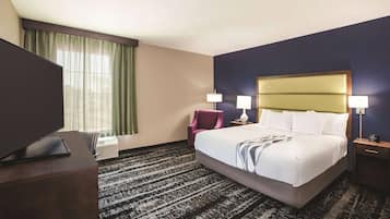 Habitación de hotel con una cama grande, dos lámparas de noche, un escritorio con televisor de pantalla plana, una silla y un ventanal con cortinas.