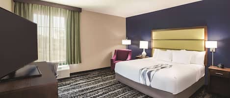 A hotel room with a large bed, two bedside lamps, a desk with a flat-screen TV, a chair, and a window with curtains.