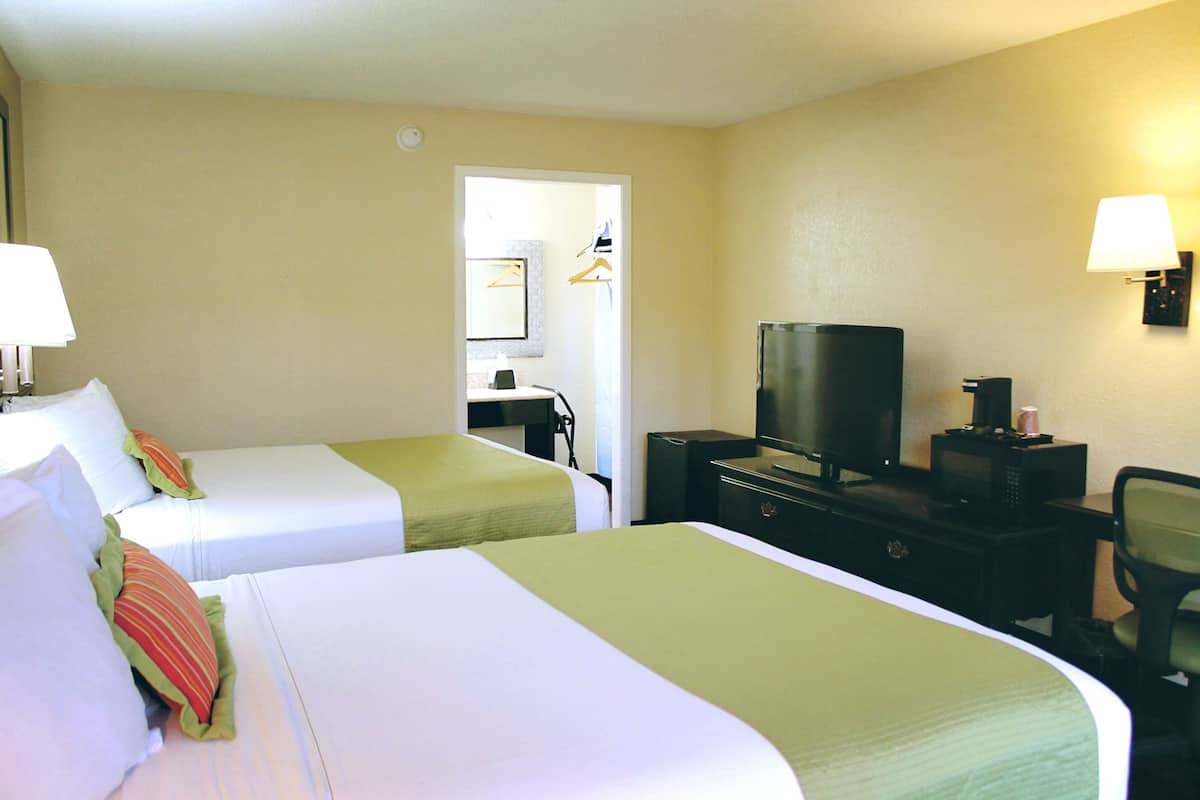 Ein Hotelzimmer mit zwei Betten, einem Schreibtisch, einem Fernseher und einem Sessel.