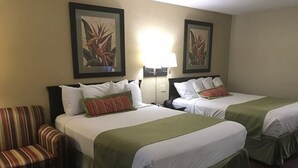 A hotel room with two beds, a striped armchair, and two framed botanical paintings on the wall. - Residence Hub Inn & Suites (Marianna)