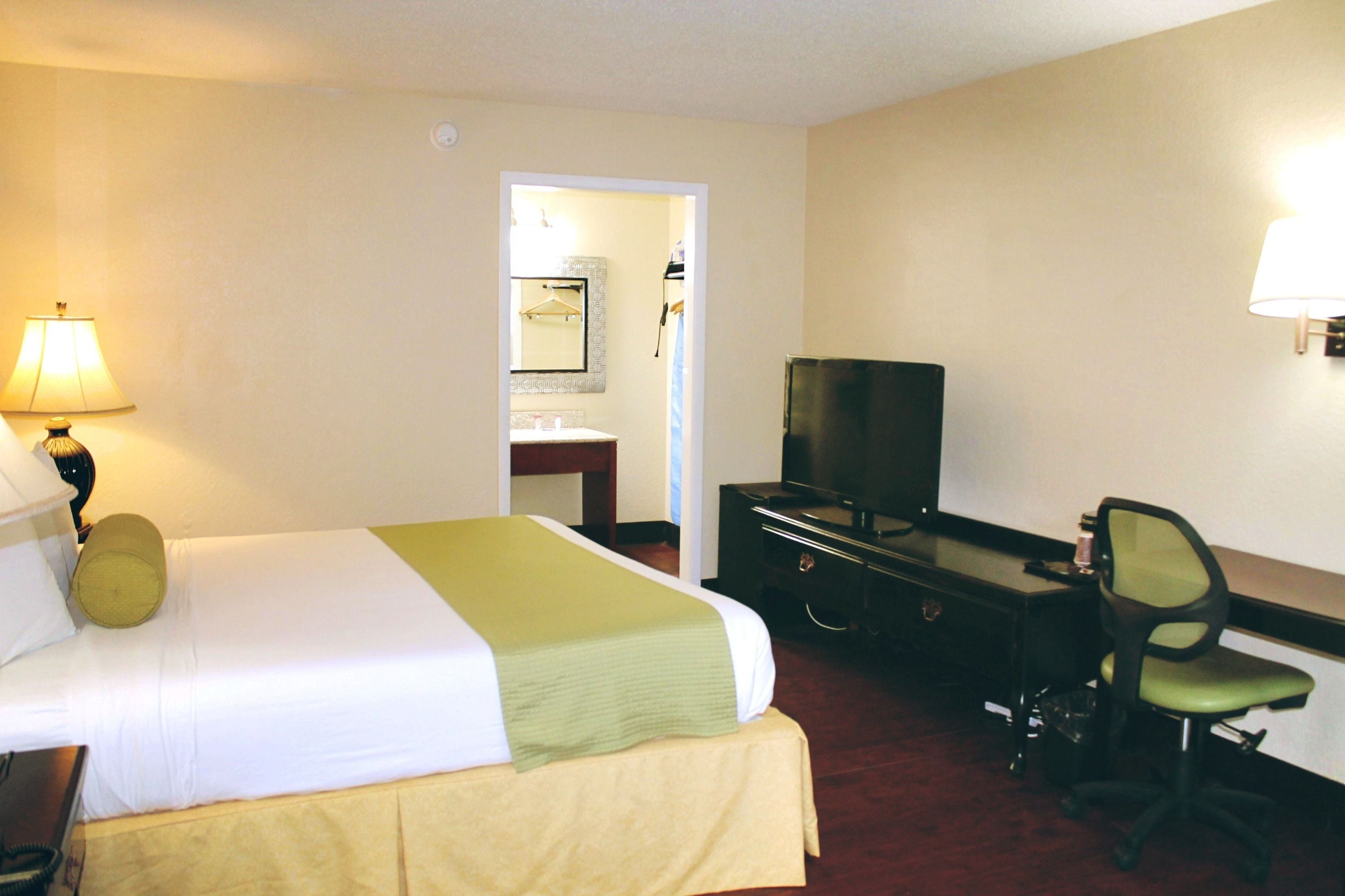 A hotel room with a bed, a desk, a chair, a television, and a lamp.