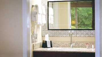 A bathroom with a marble countertop, a sink, a mirror, and a towel dispenser.