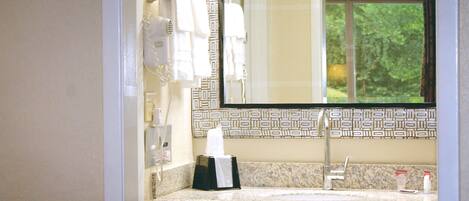 A bathroom with a marble countertop, a sink, a mirror, and a towel dispenser.