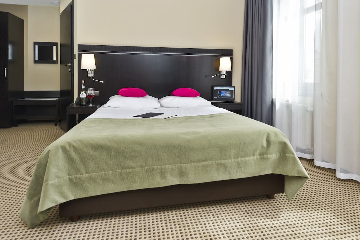A hotel room with a large bed, two bedside lamps, a TV, and a window with curtains.