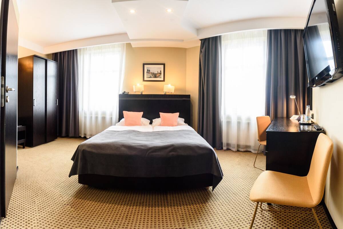 A hotel room with a large bed, a desk, and a TV on the wall.