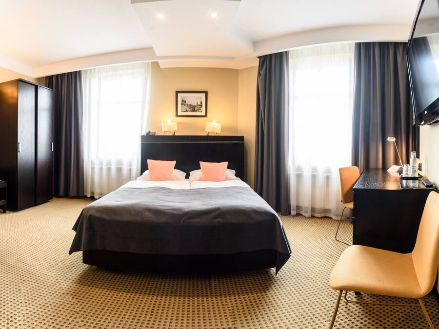 Habitación de hotel con una cama grande, un escritorio y un televisor en la pared.