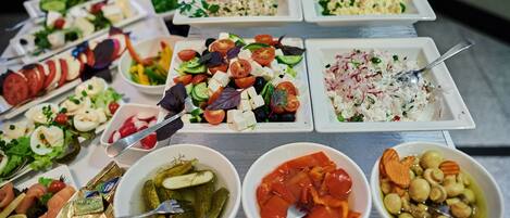 Un bufé con diversos platos, incluyendo ensaladas, quesos y encurtidos.