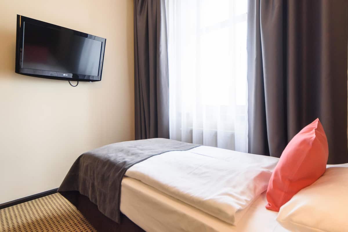 A hotel room with a bed, a television mounted on the wall, and a window with curtains.