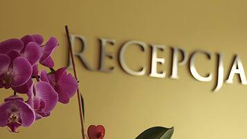 A reception sign with the word "RECEPCJA" in large letters, accompanied by a purple orchid and a heart-shaped decoration.