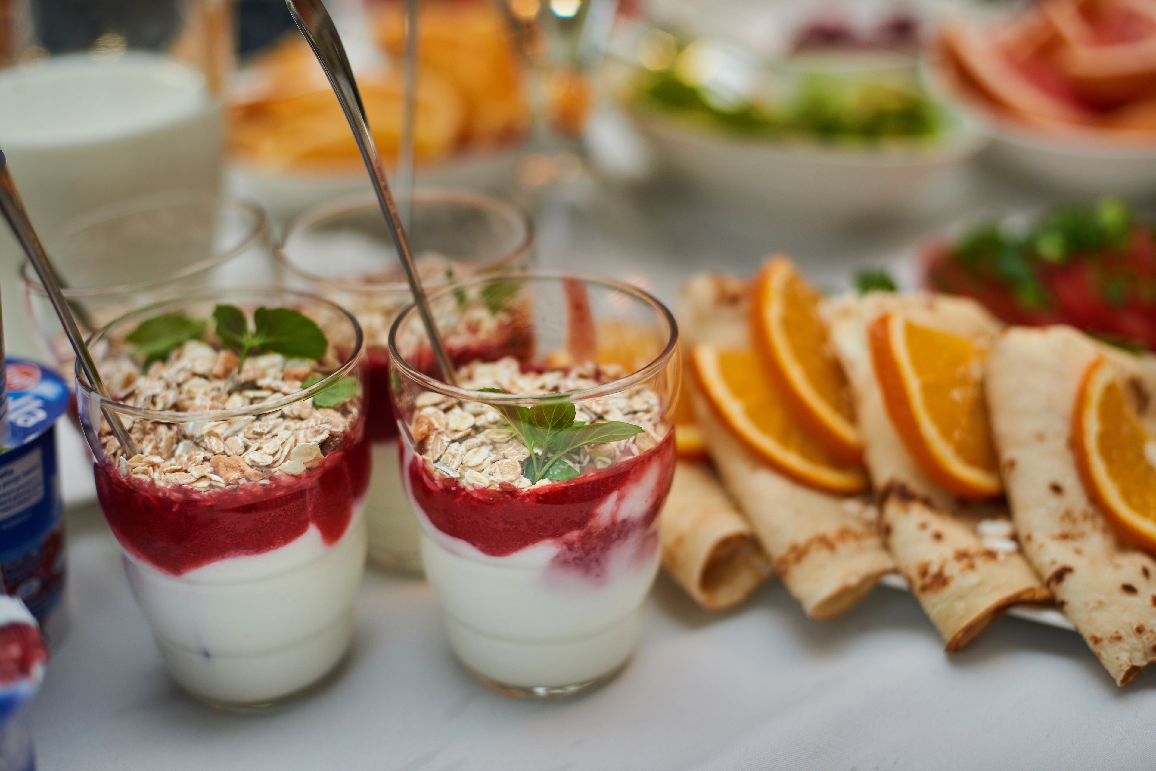 A dessert table with layered parfaits, orange slices, and rolled pastries.