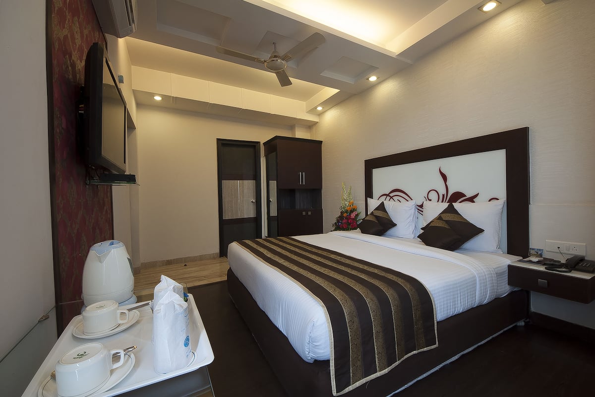 Habitación de hotel con una cama grande, una mesita de noche con teléfono y lámpara, un ventilador de techo y un televisor montado en la pared.
