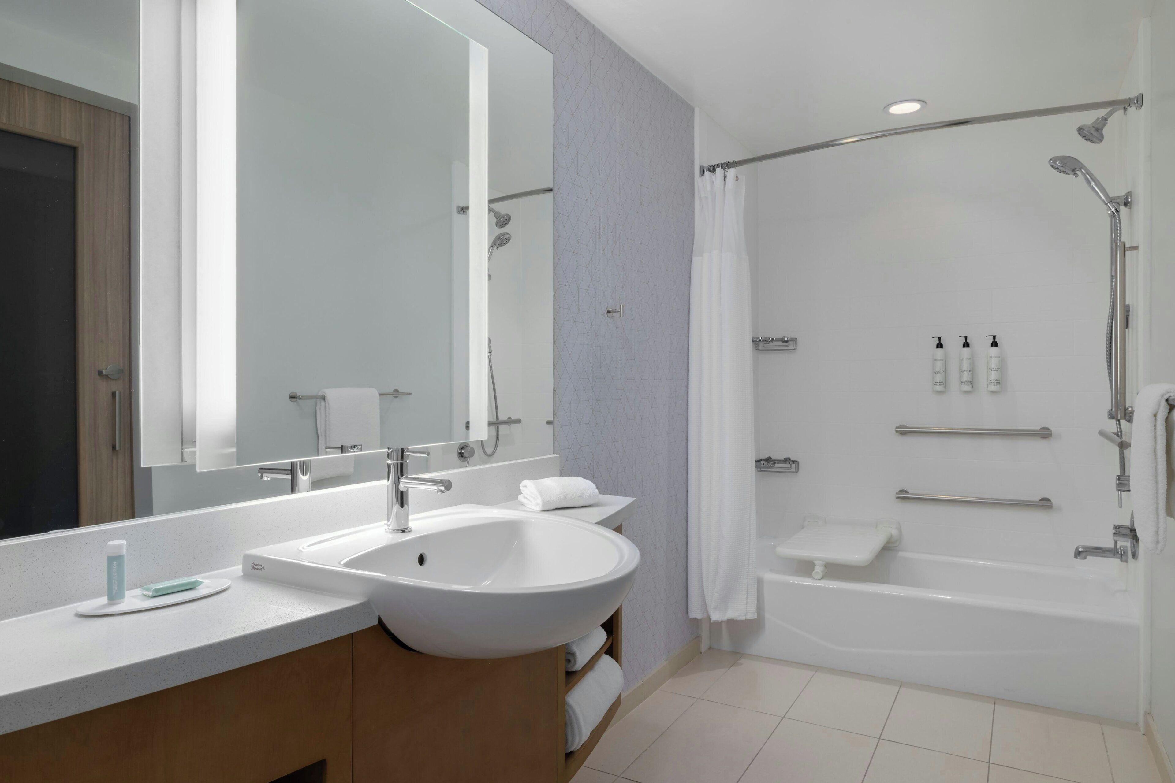 Un baño moderno con un espejo grande, un lavamanos blanco, una bañera y una zona de ducha.