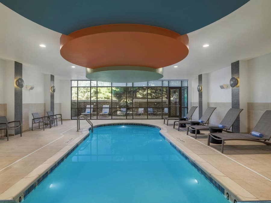 A swimming pool with lounge chairs and a view of trees through large windows.