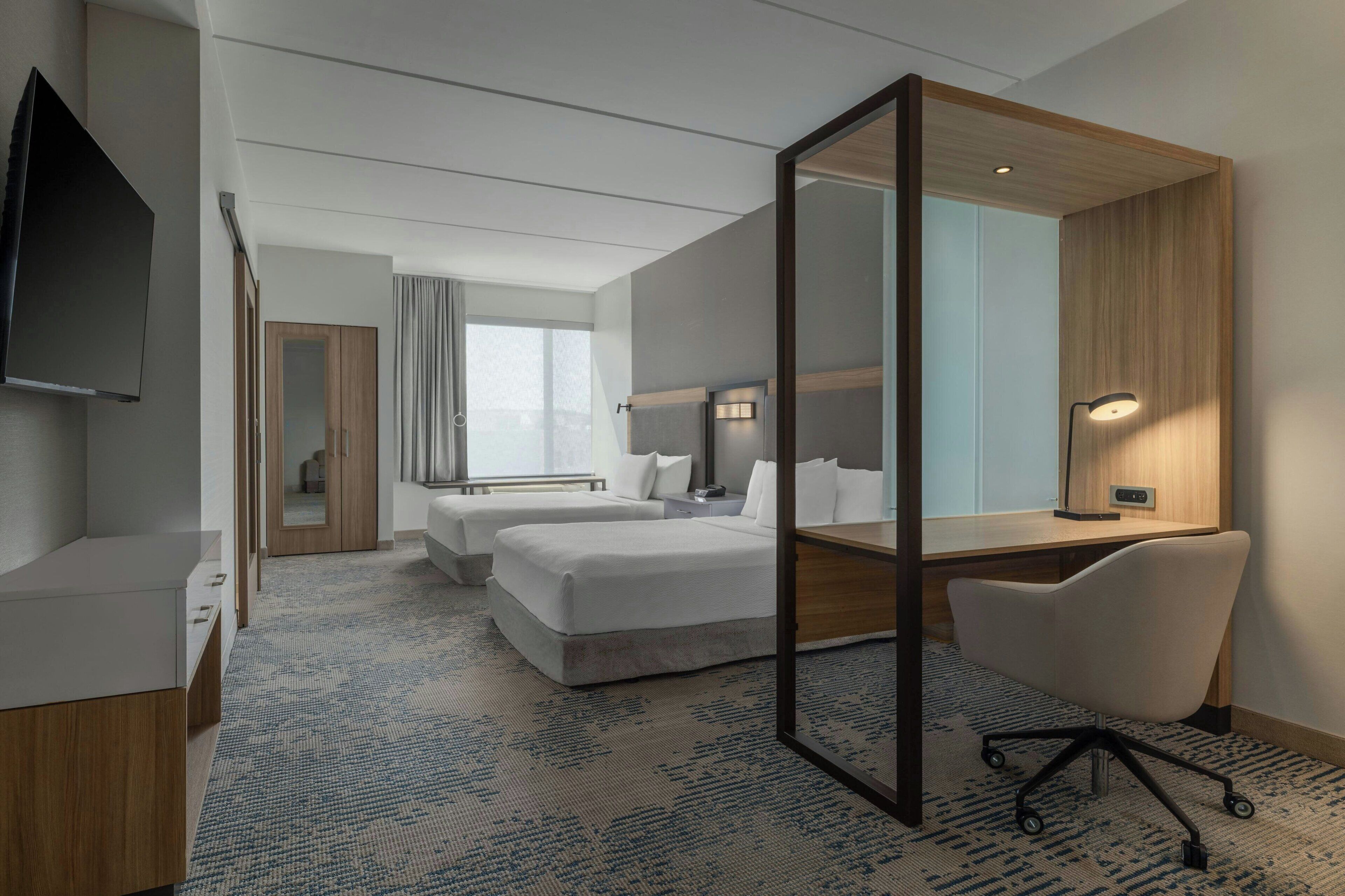 A hotel room with a bed, desk, chair, and a TV.