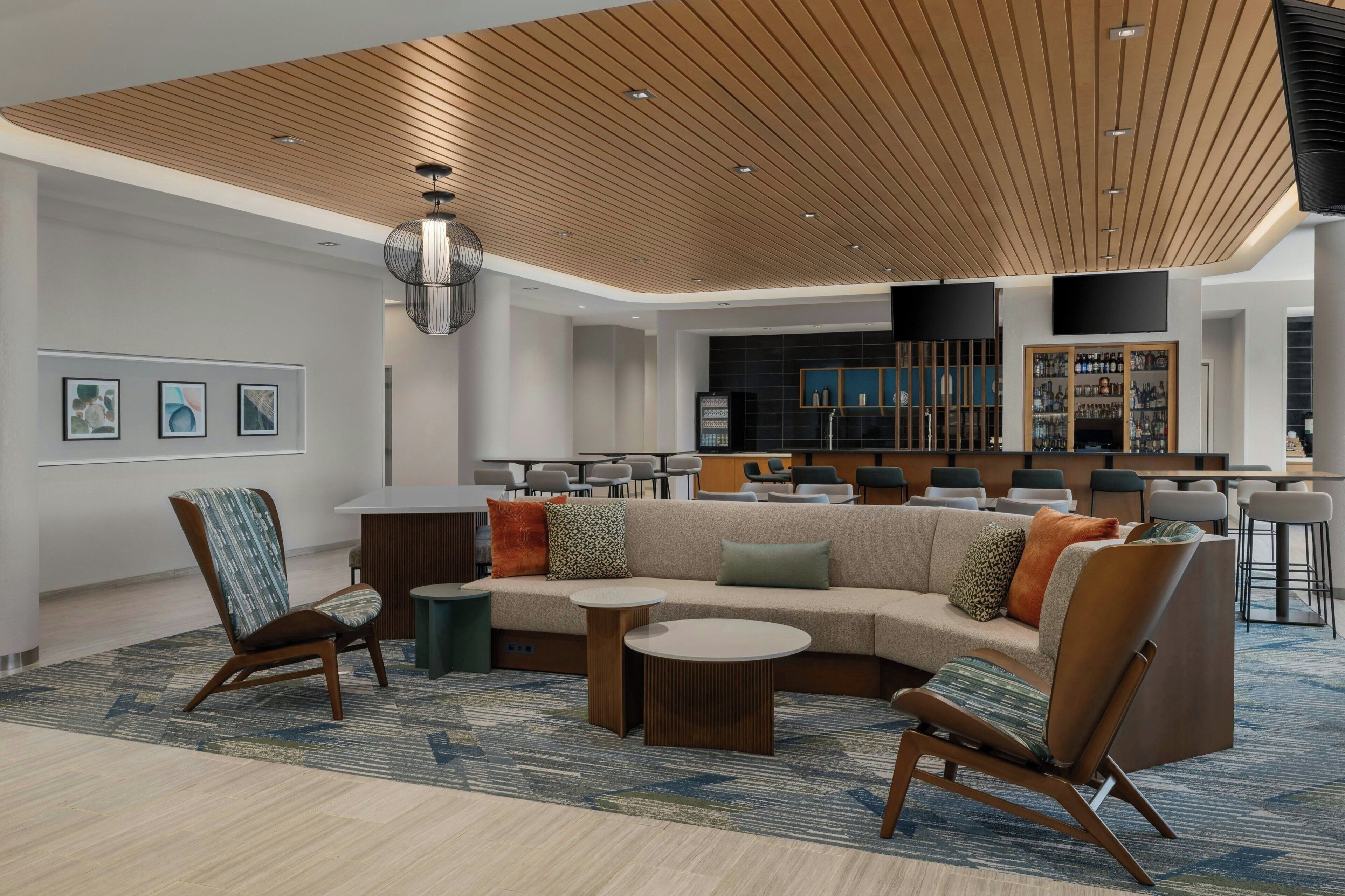 A modern lounge area with a sectional sofa, armchairs, a coffee table, and a bar area in the background.