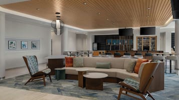 A modern lounge area with a sectional sofa, armchairs, a coffee table, and a bar area in the background.