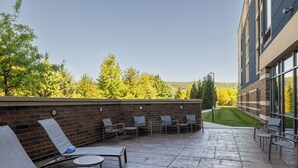 Un espacio al aire libre con sillones de descanso y un muro de ladrillo, con vista a un área verde y árboles.