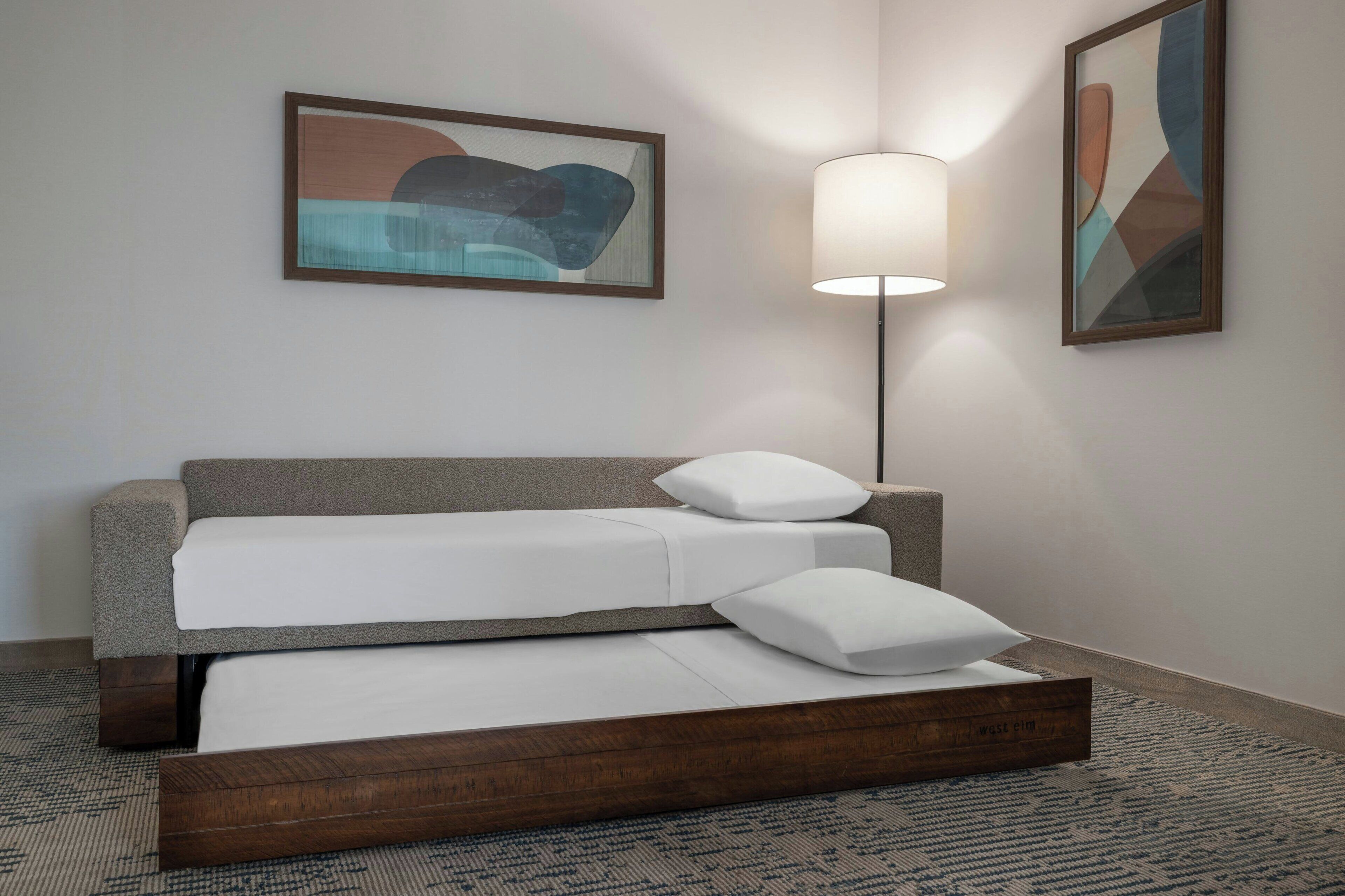 A hotel room with a bed, a wall-mounted lamp, and two framed artworks.