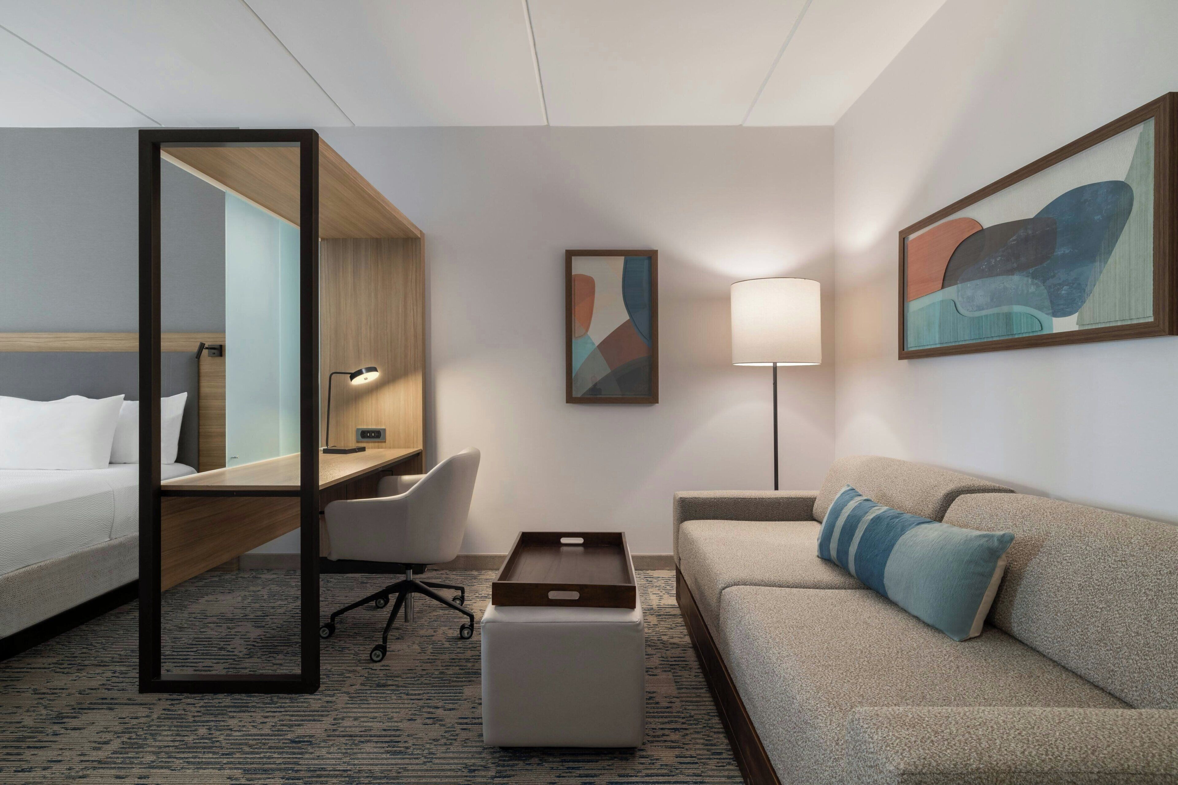 A hotel room with a bed, a desk, a chair, a sofa, a coffee table, and artwork on the walls.