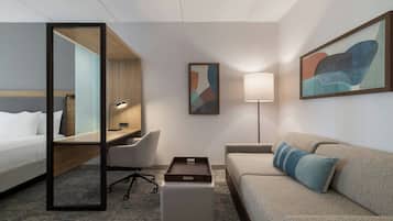 A hotel room with a bed, a desk, a chair, a sofa, a coffee table, and artwork on the walls.