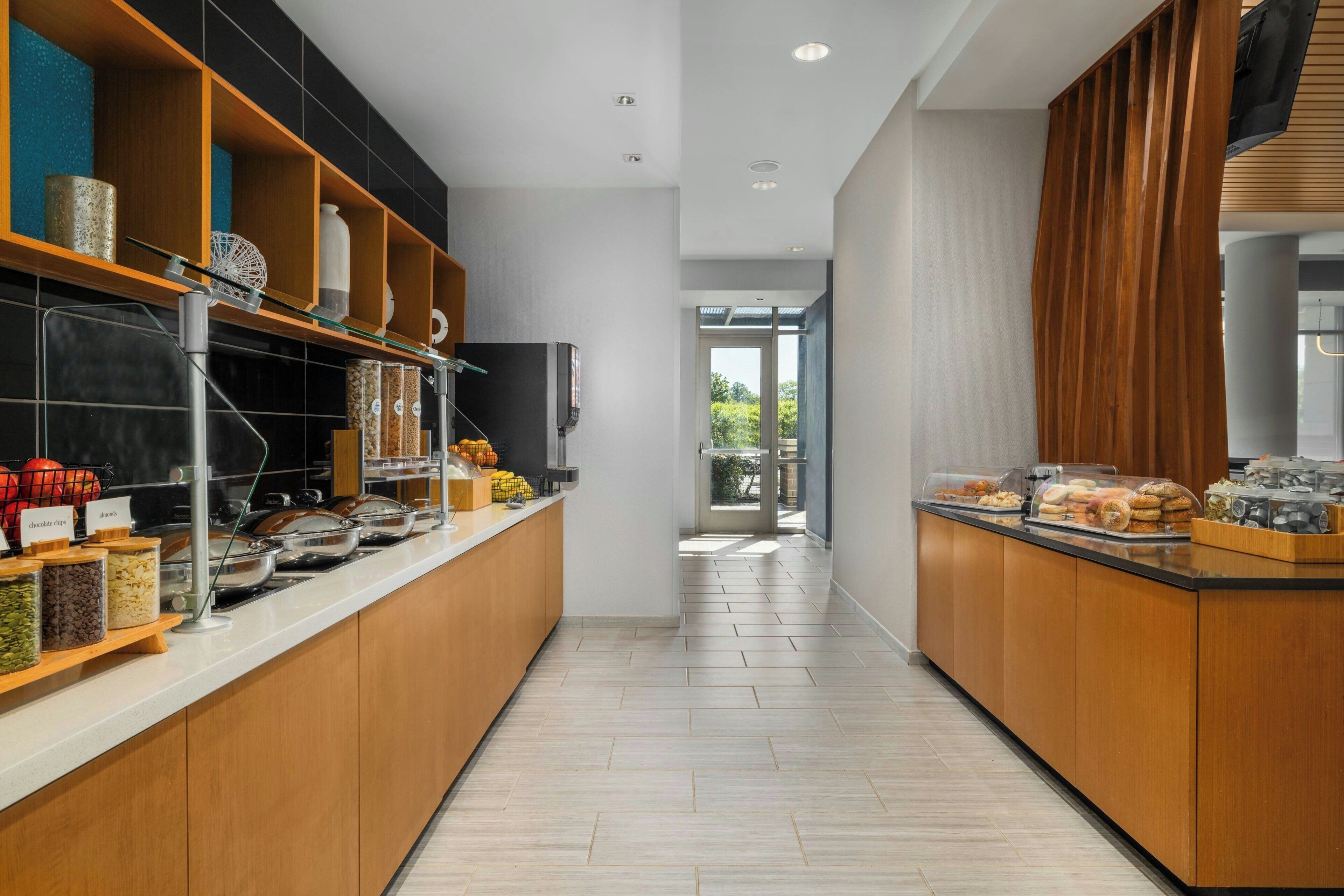 A modern kitchen with a long counter, various food dispensers, and a view to the outdoors.