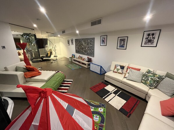 A modern living room with a sofa, a green and red striped tent, and a cityscape wall art.