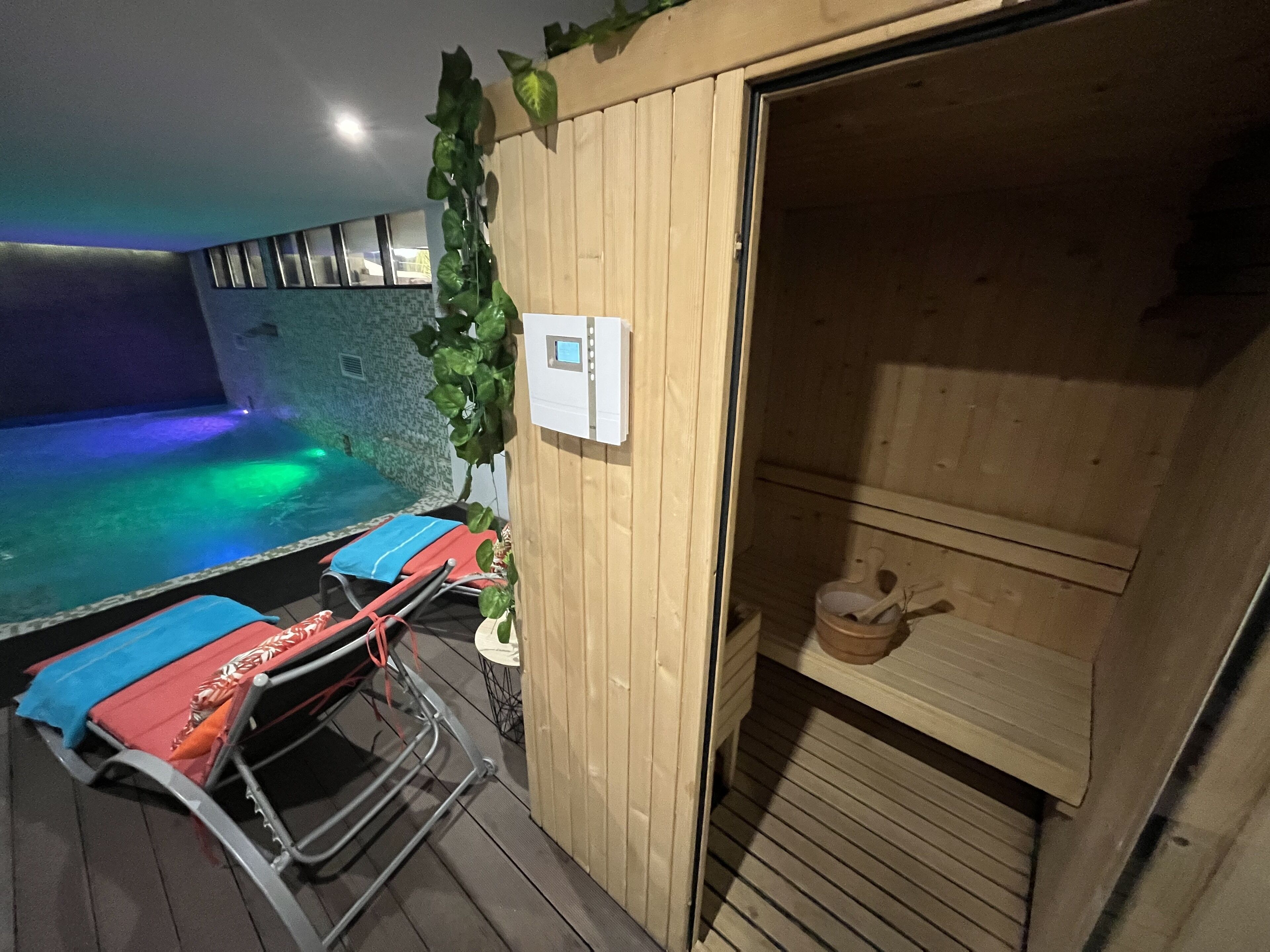 A sauna room with a wooden bench, a small table with a teapot, and a control panel on the wall.