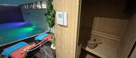 A sauna room with a wooden bench, a small table with a teapot, and a control panel on the wall.