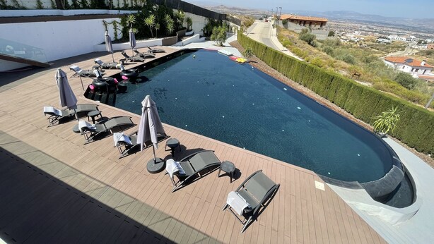 A rooftop pool with lounge chairs and umbrellas, surrounded by a high wall and a view of the city.