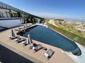 Piscina en la azotea con sillones de descanso y sombrillas, rodeada por un muro alto y con vista a la ciudad.