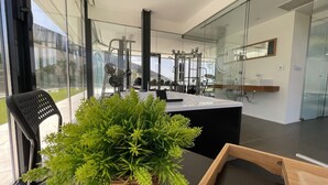 A modern hotel room with a large window, a view of the outdoors, a black chair, a wooden table, and a potted plant.