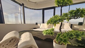 A modern bedroom with a large bed, a potted plant, and rolled towels on a dark wooden table.