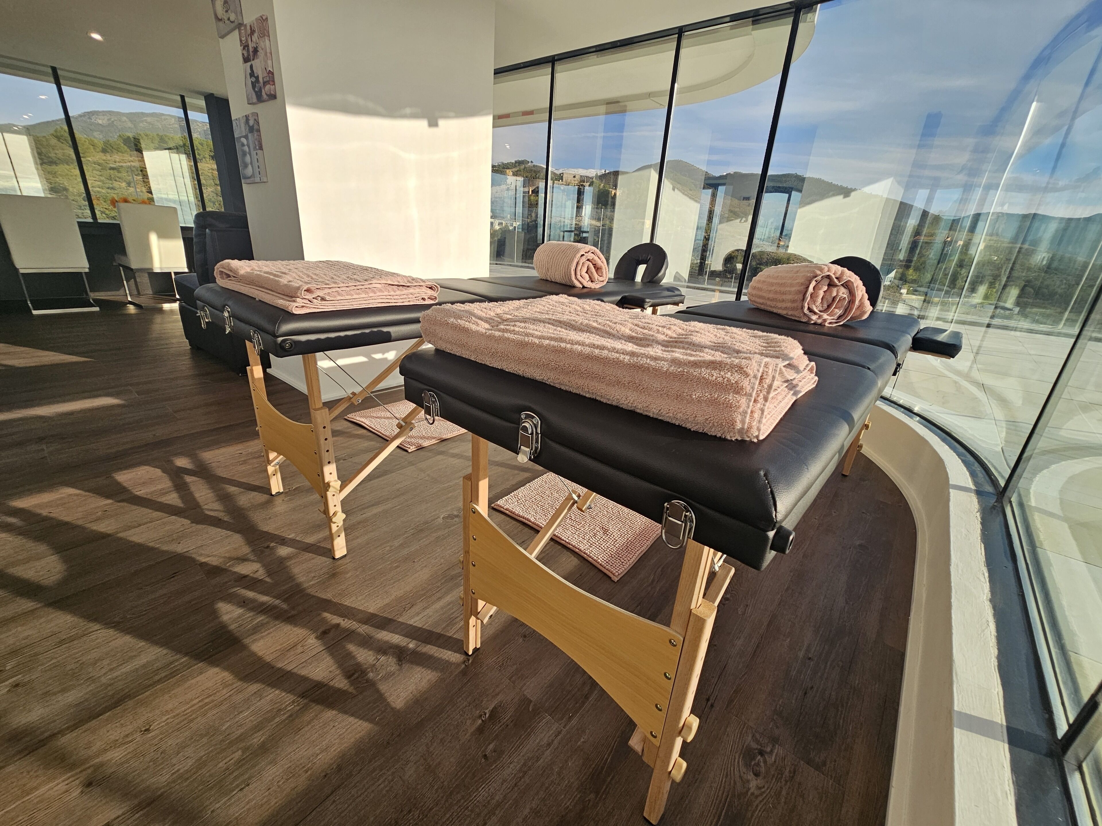 Een massageruimte met twee massagetafels, houten voetenbankjes en handdoeken.