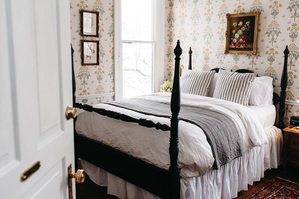 Un dormitorio con cama con dosel, papel tapiz floral y un cuadro en la pared.