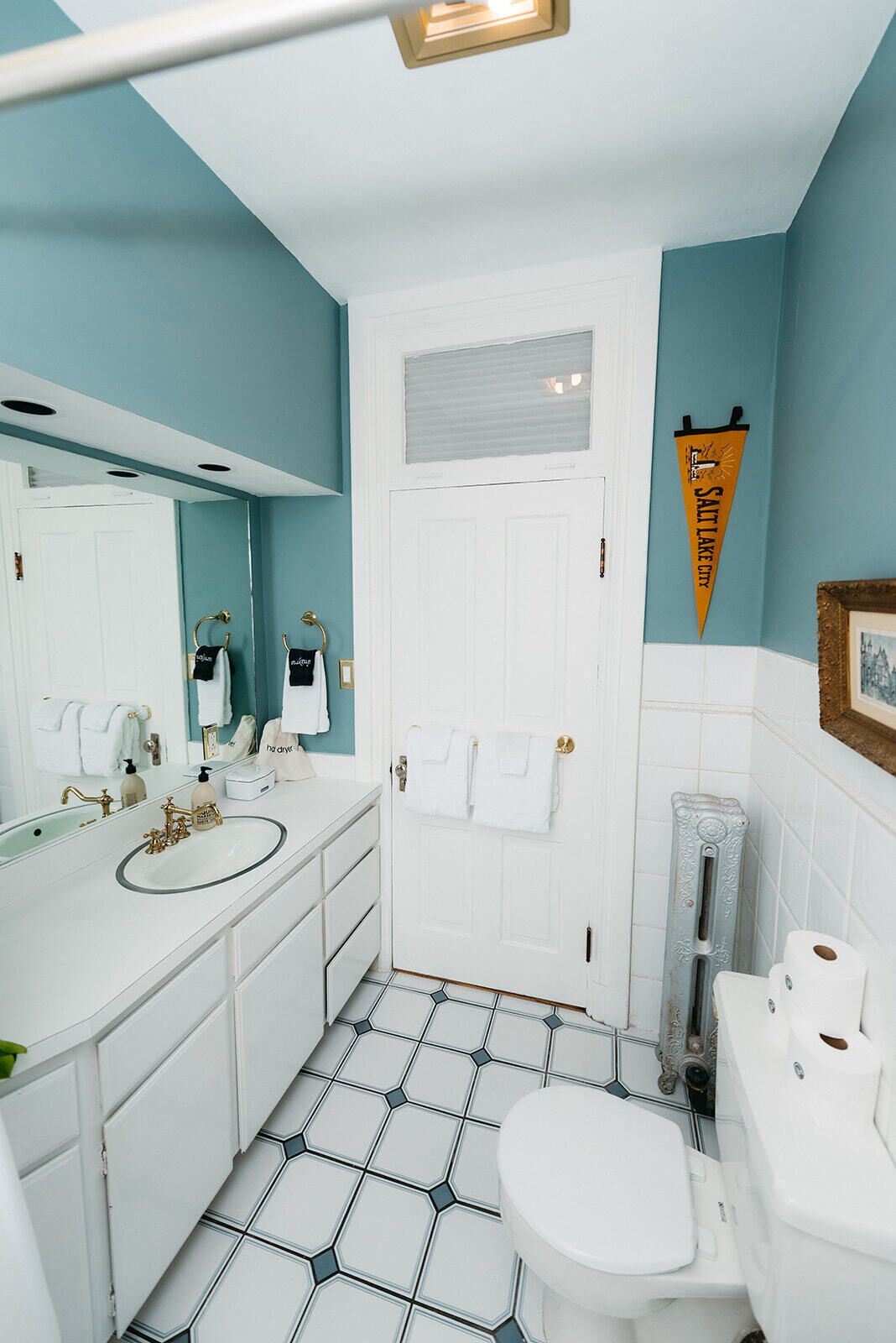 A bathroom with a white sink, a toilet, and a shower area. There is a towel rack with towels hanging on it, and a towel hanging on the door. The floor has a geometric tile pattern.