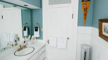 A bathroom with a white sink, a toilet, and a shower area. There is a towel rack with towels hanging on it, and a towel hanging on the door. The floor has a geometric tile pattern.