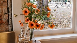 Una cocina con una tabla de cortar de madera que sostiene un tarro con la etiqueta 'Cuisinart' y un florero con flores naranjas.