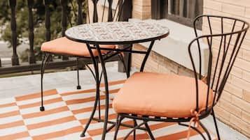 Een balkon met een zwart-wit geruite vloer, twee metalen stoelen met kussens, en een kleine ronde tafel.