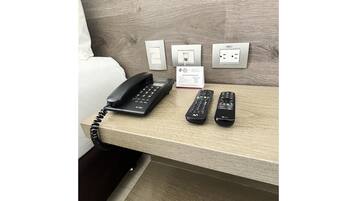 A hotel room with a wooden headboard, a telephone, and two remote controls on a wooden table.