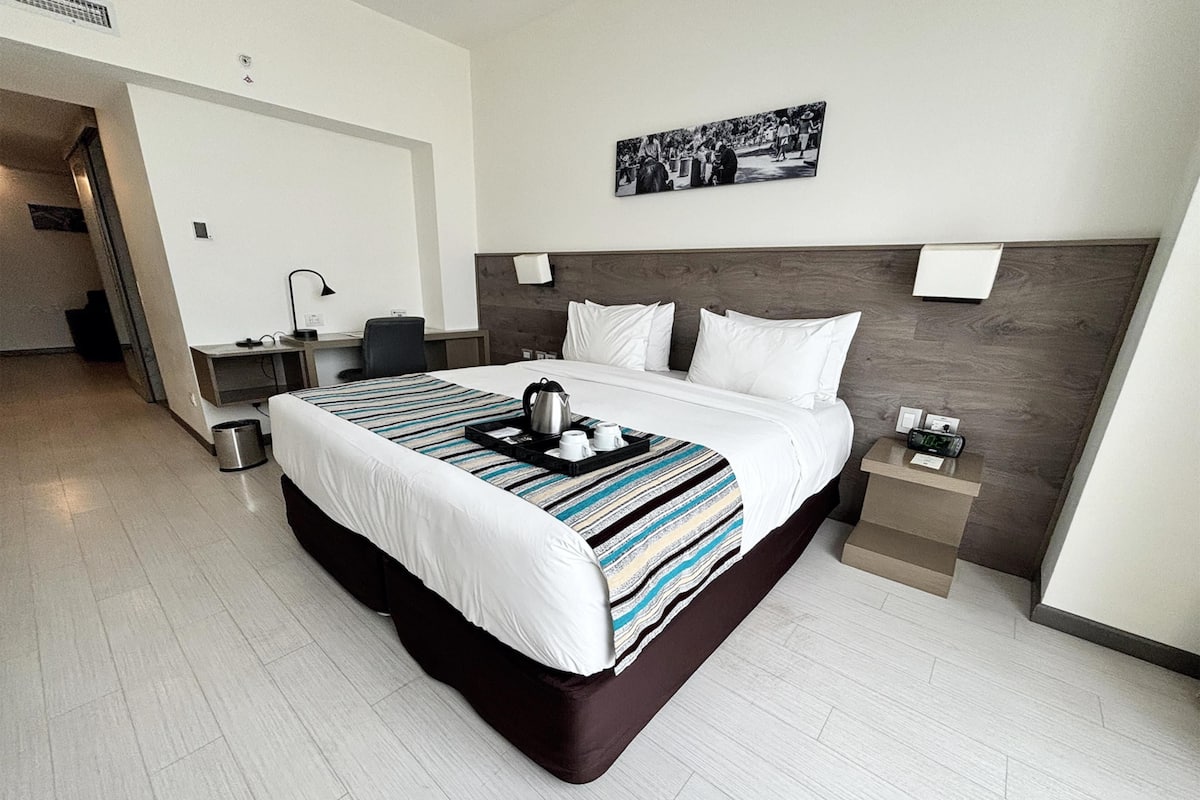 Quarto de hotel moderno com uma cama grande, uma escrivaninha e uma mesa de cabeceira.
