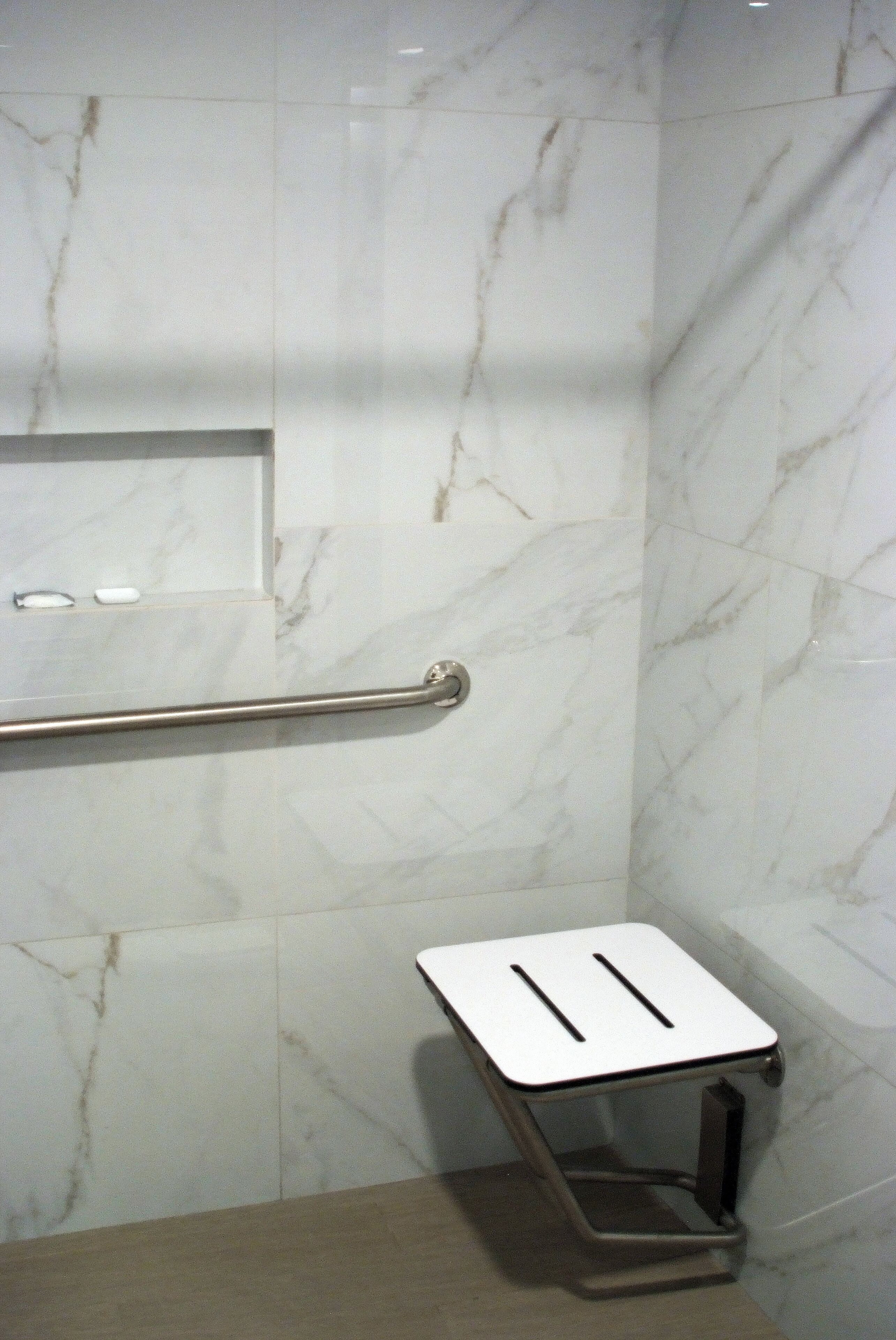 A bathroom with marble walls, a handrail, and a small white sink with a mirror.