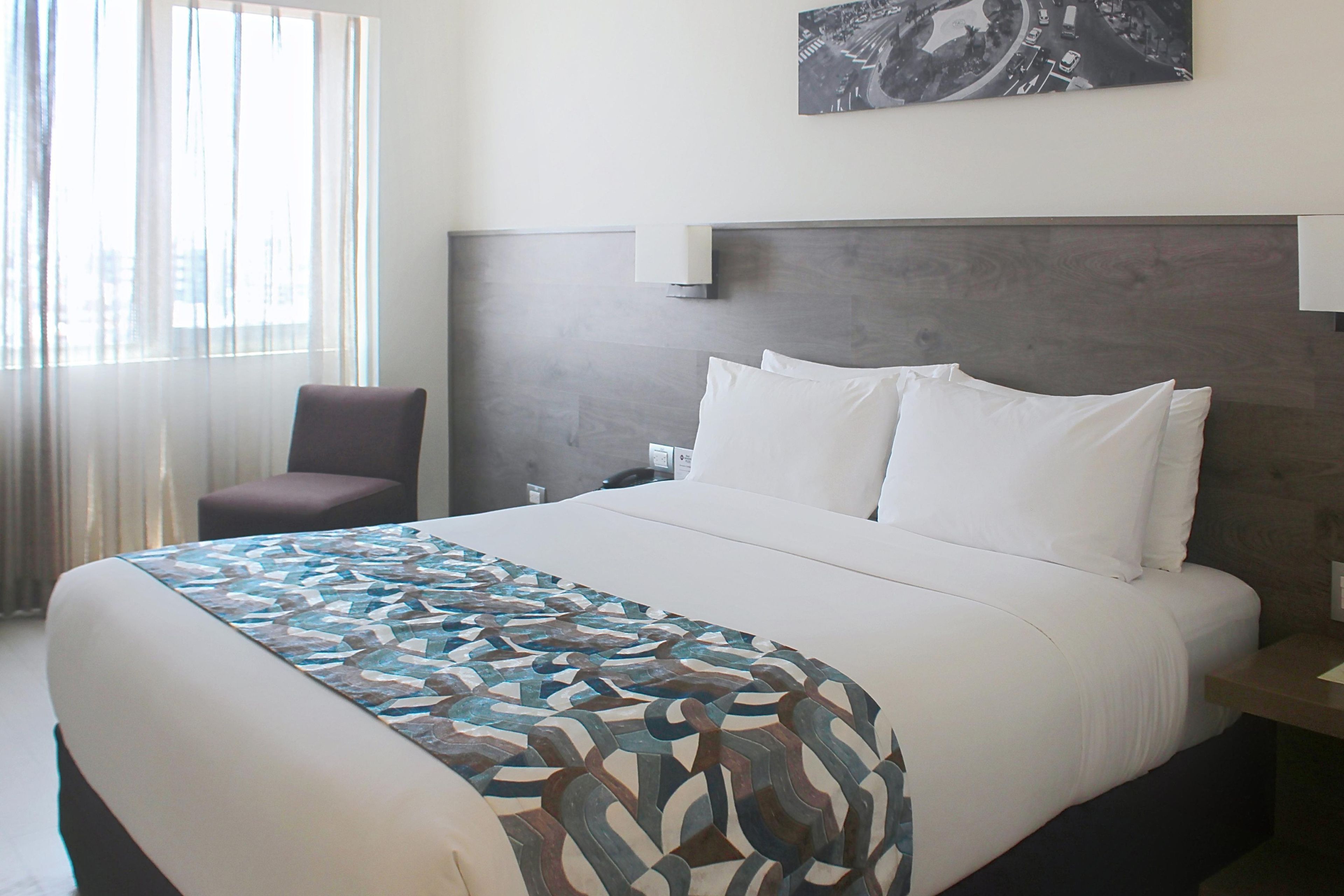 Ein Hotelzimmer mit einem großen Bett, einem Sessel, einem Nachttisch und einer Wandlampe.