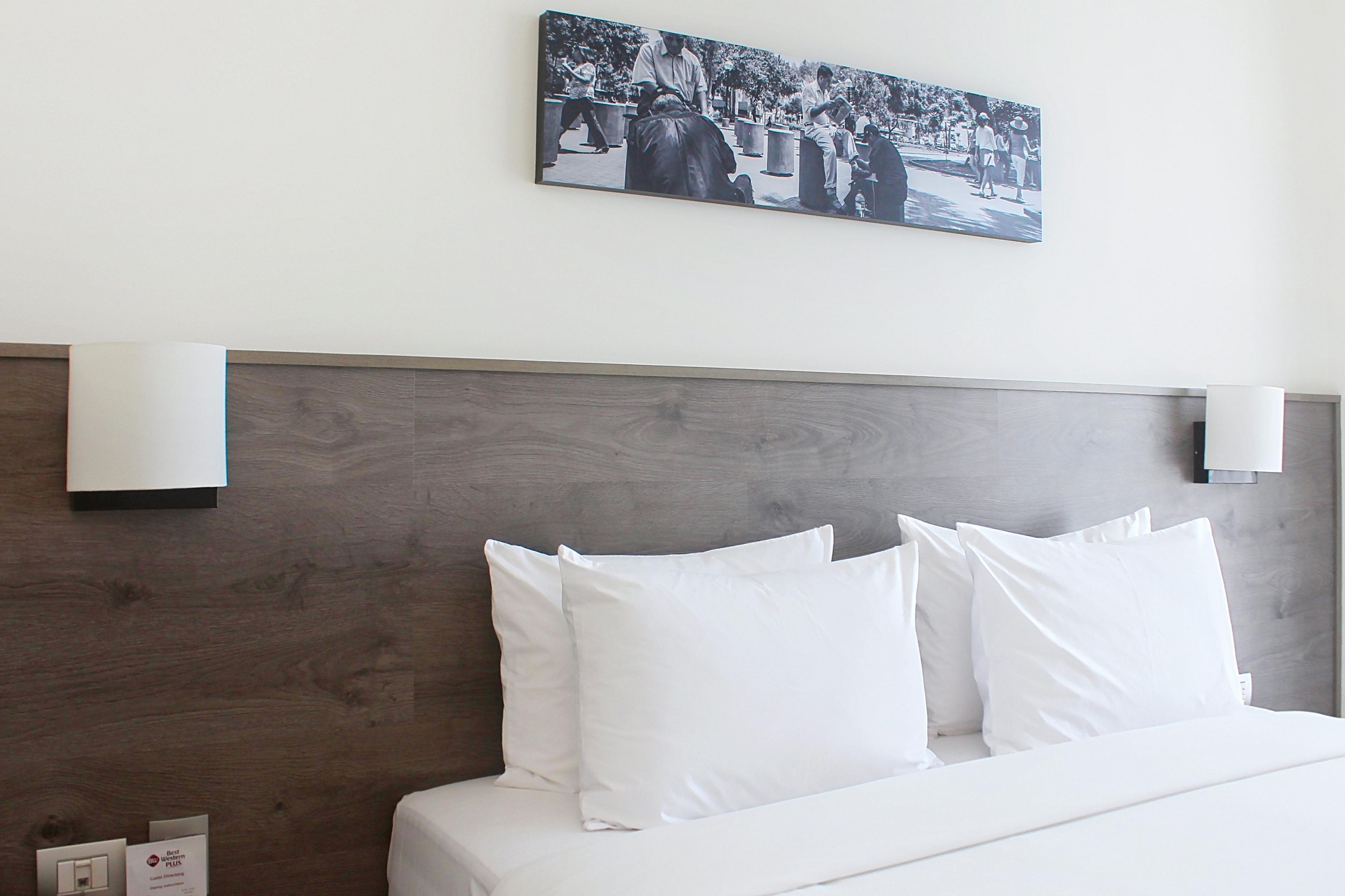 Une chambre d’hôtel avec une tête de lit en bois, du linge de lit blanc et une photographie encadrée accrochée au mur.