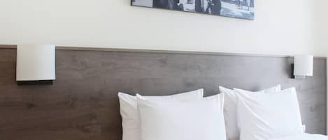 Une chambre d’hôtel avec une tête de lit en bois, du linge de lit blanc et une photographie encadrée accrochée au mur.